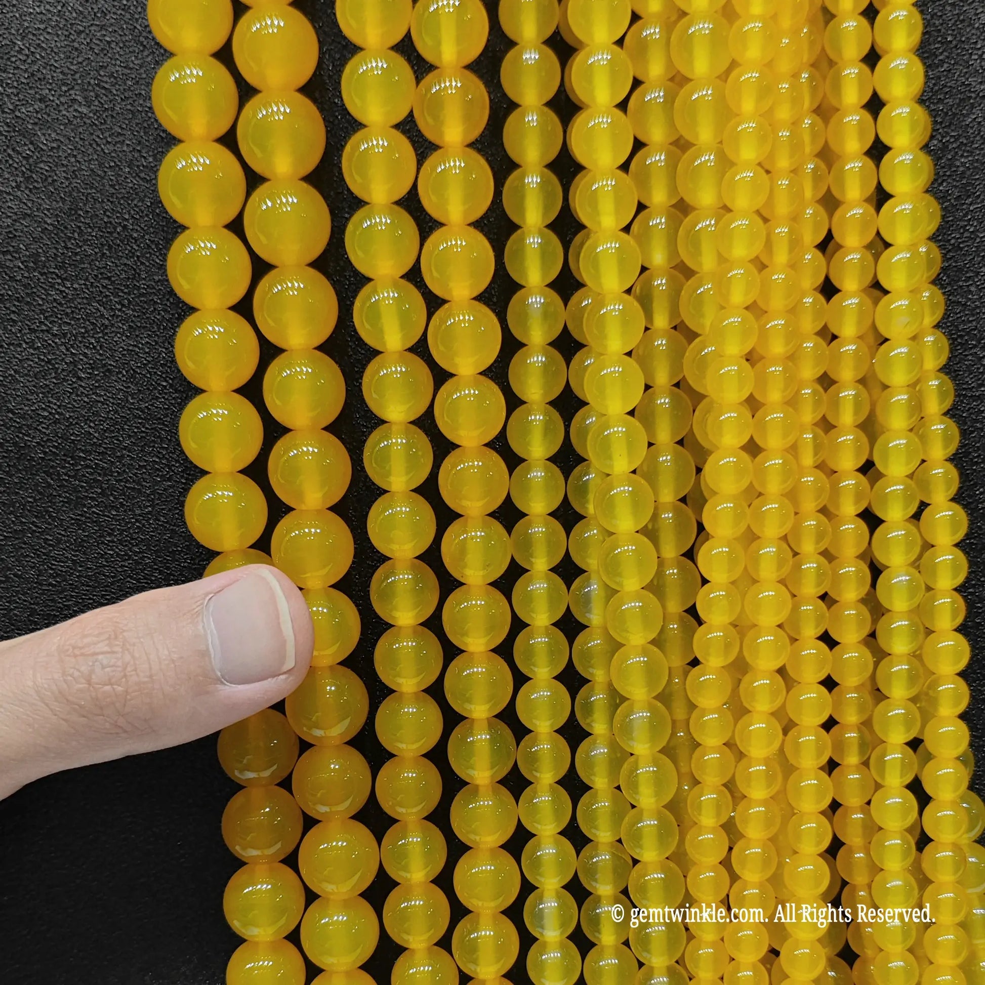 A full bunch of yellow agate round beads from 4mm to 14mm held in hand for studio stock inspection