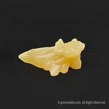 Side angle of a hand carved yellow calcite cute axolotl stone statue on a plain dark background