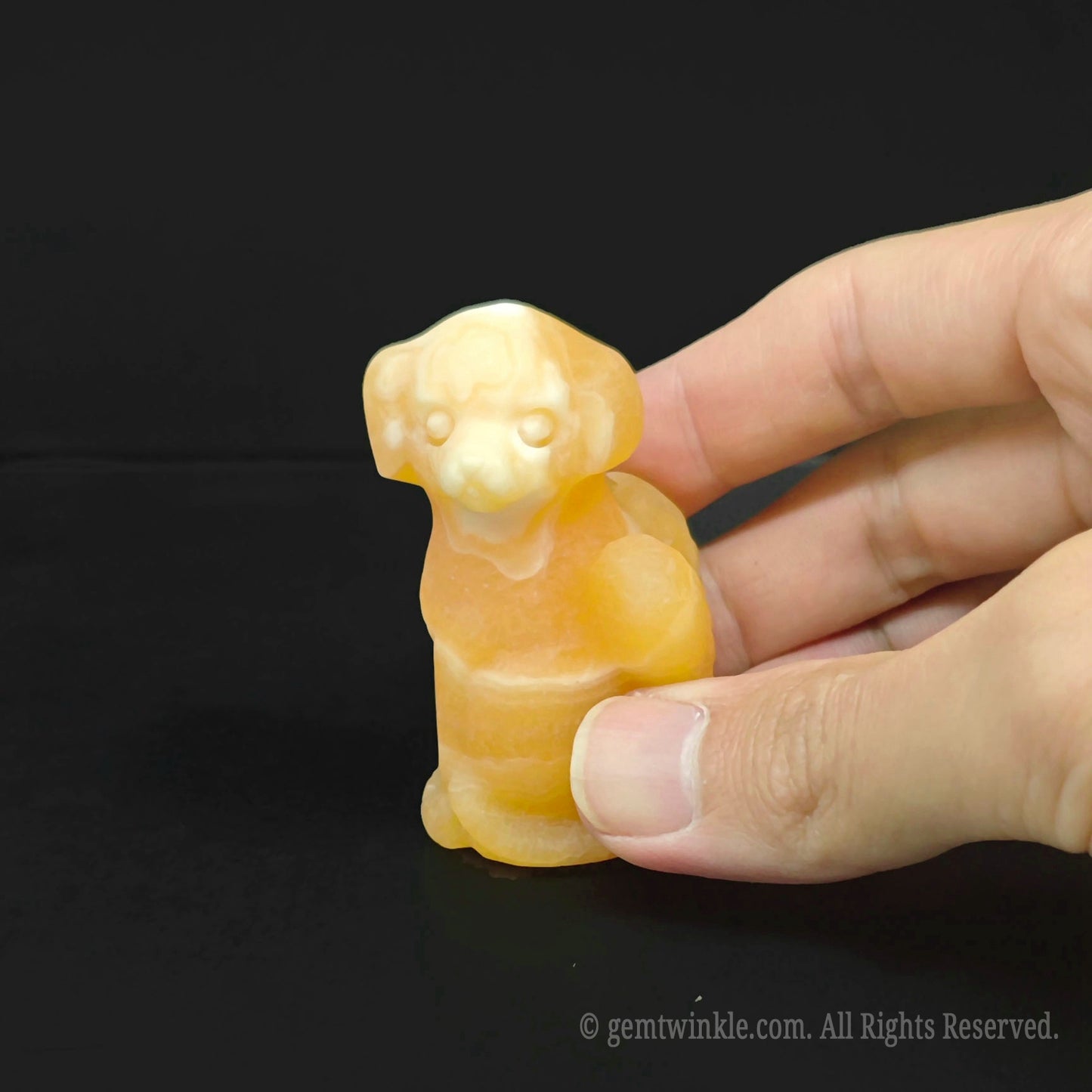 Warm honey yellow calcite winged puppy statue held in hand showcasing glossy transparency for boutique inventory