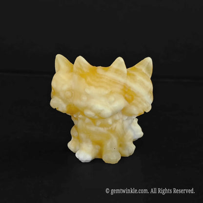 A standalone front view of a golden yellow calcite chibi Cerberus sculpture displaying warm mineral bands and triple head alignment