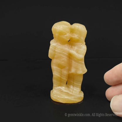 Warm honey yellow calcite kissing couple statue resting on a black surface for boutique store inventory