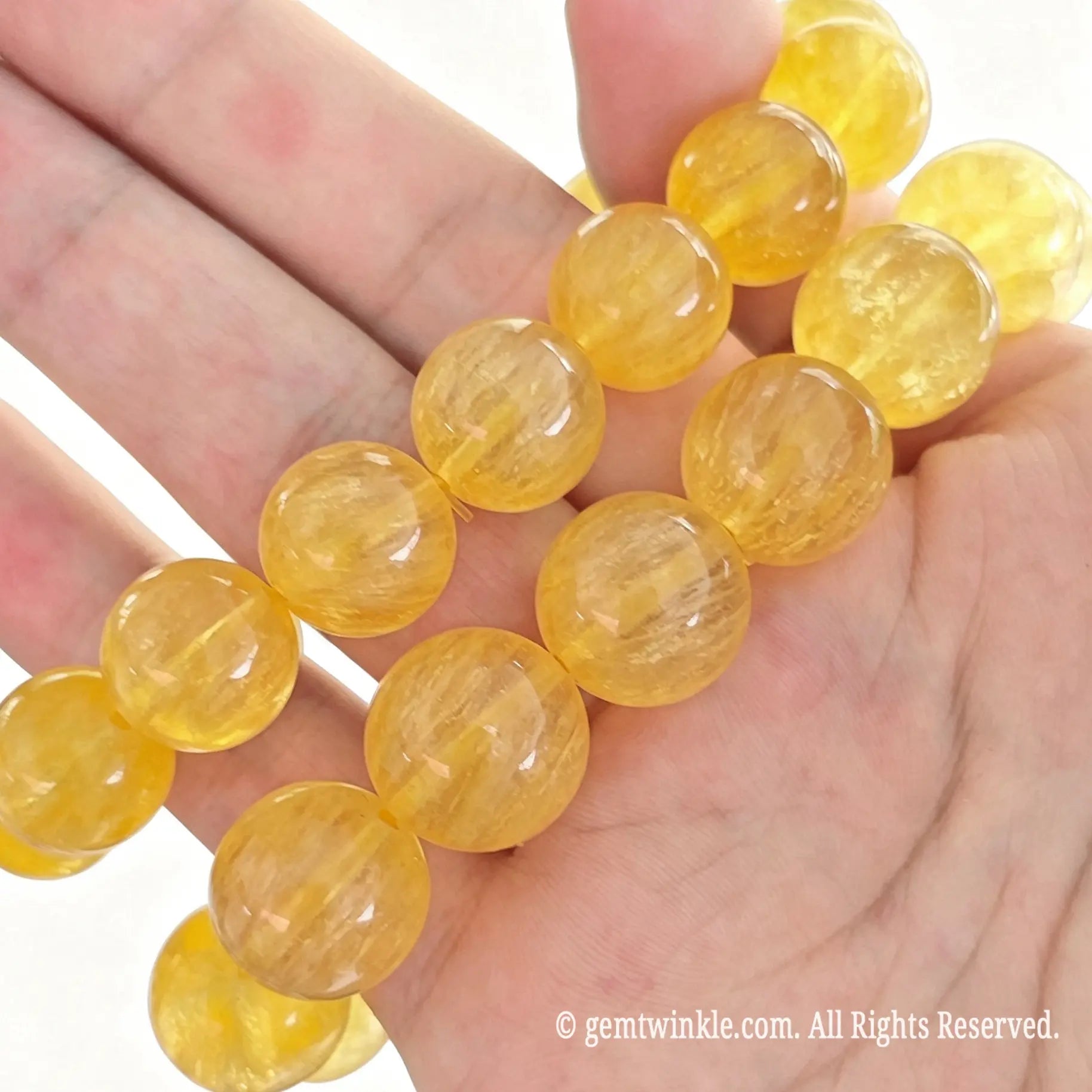 Handheld angle view of yellow silk fluorite round bead stretch bracelets showing glossy polish and subtle cat eye striations