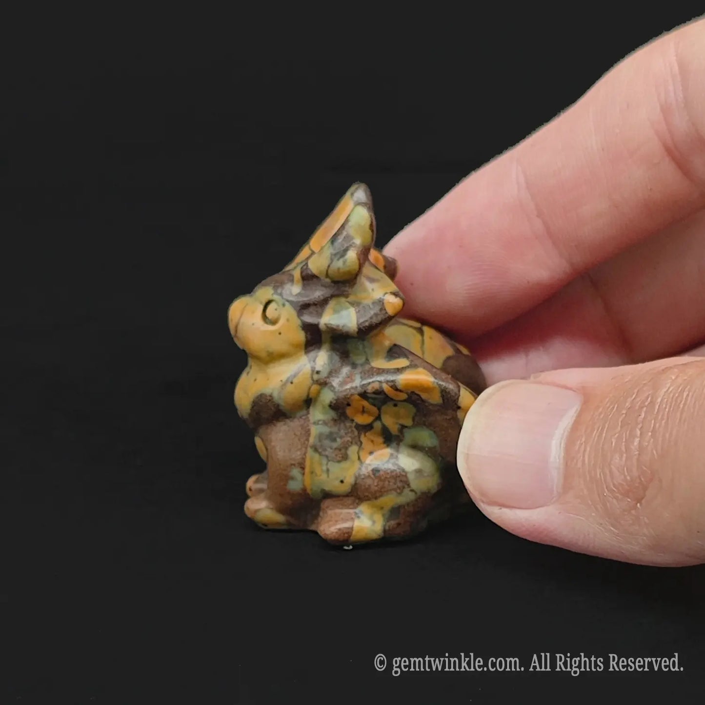 Handheld view of a 3cm yellow jasper patterned mythical winged horn beast carving demonstrating retail scale