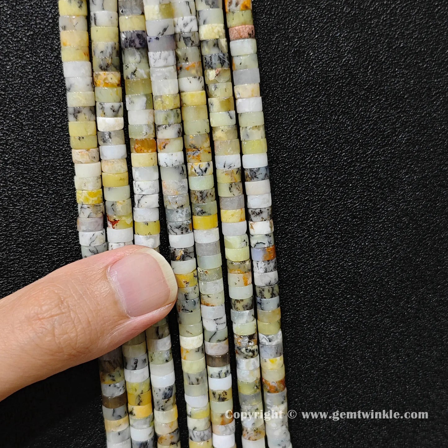 Close up view of 6x3mm yellow opal disc rondelle beads inspected on fingers for quality preview