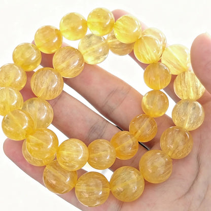 Main view of yellow silk fluorite round bead stretch bracelets arranged in a loop on open palm showing transparent golden color and silky chatoyant texture