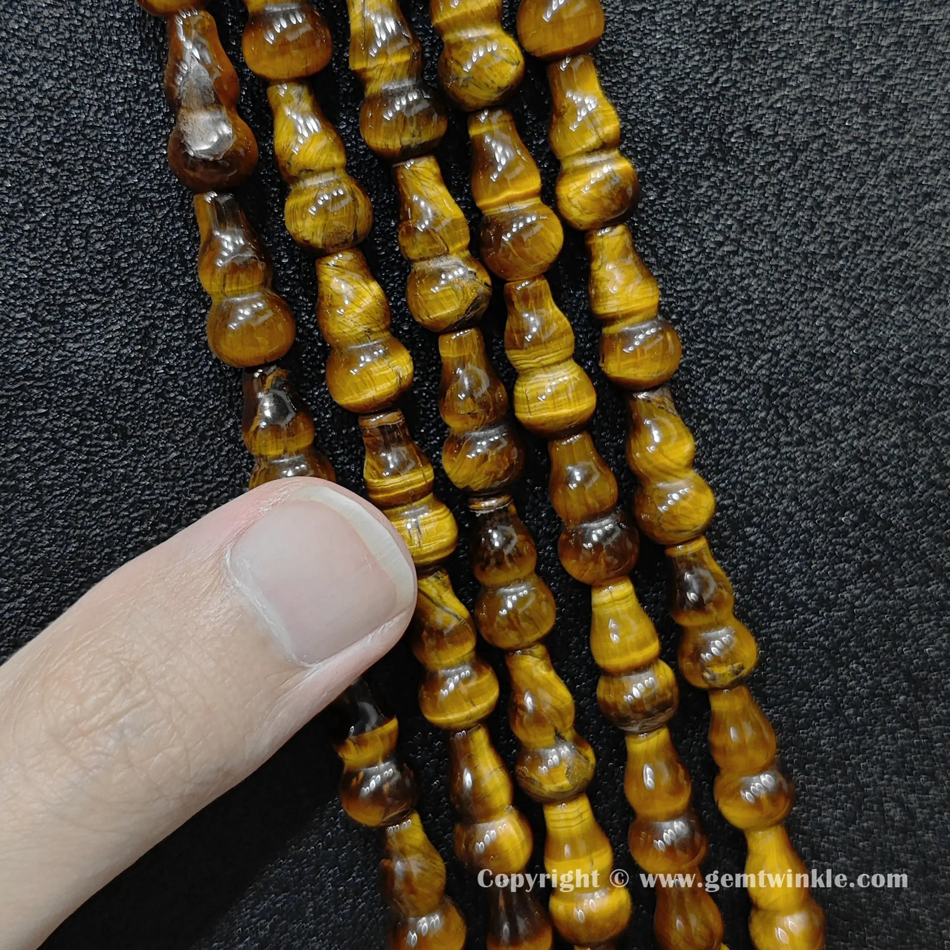 Natural yellow tiger eye gourd bead strand held over hand showing size scale