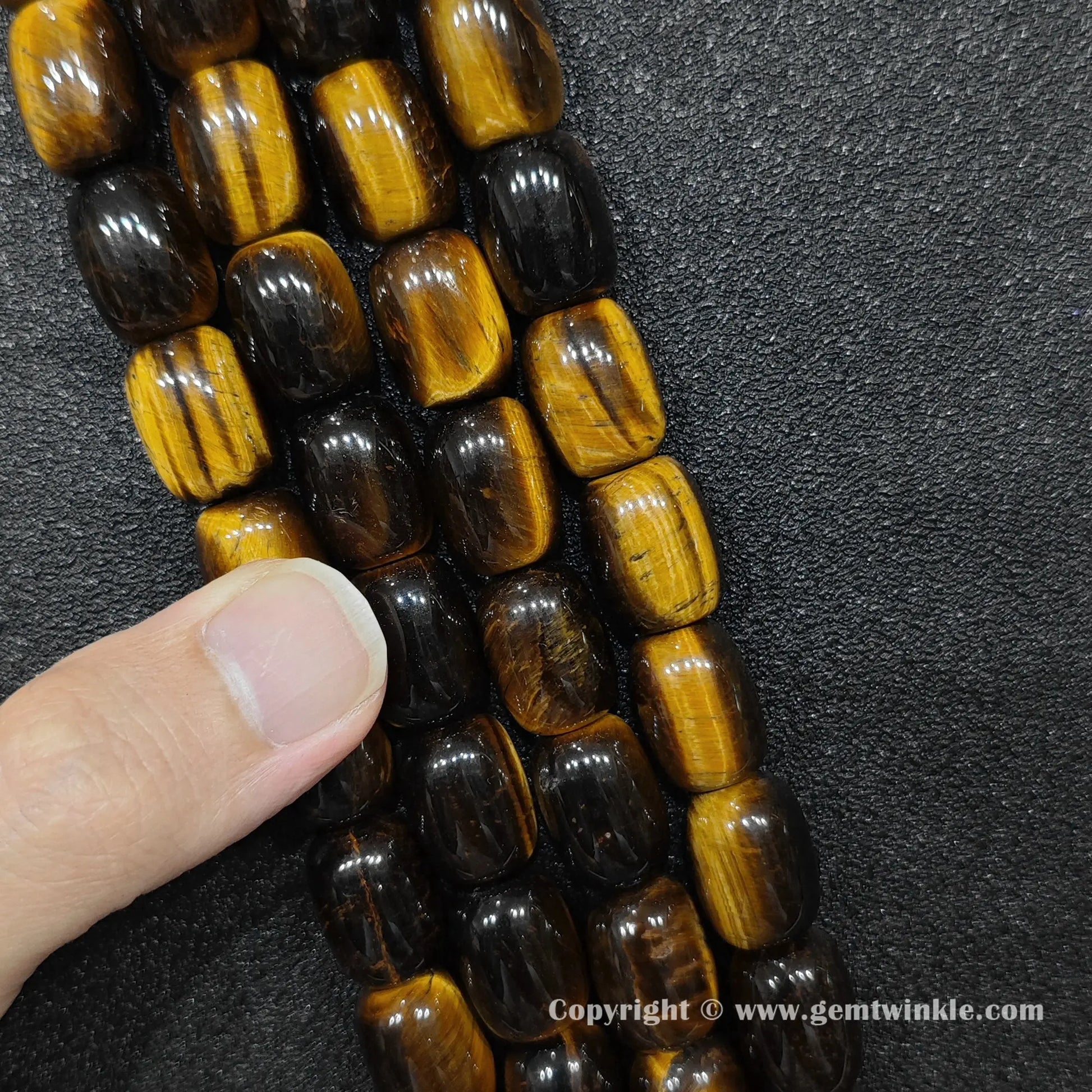 Natural yellow tigers eye barrel bead strand held over hand for size scale