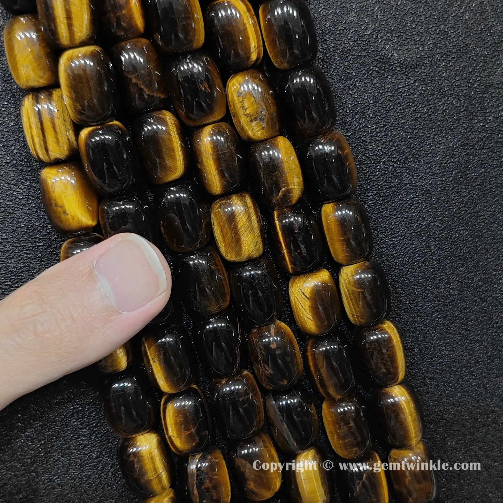 Close up view of natural yellow tigers eye cylinder beads on hand showing strand quality