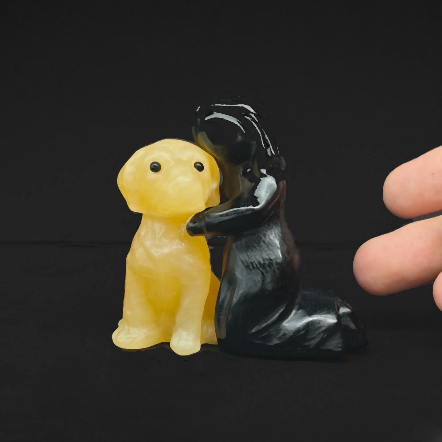 Opposite view of the hand carved yellow calcite puppy held by a black obsidian owner highlighting polished mineral texture and scale
