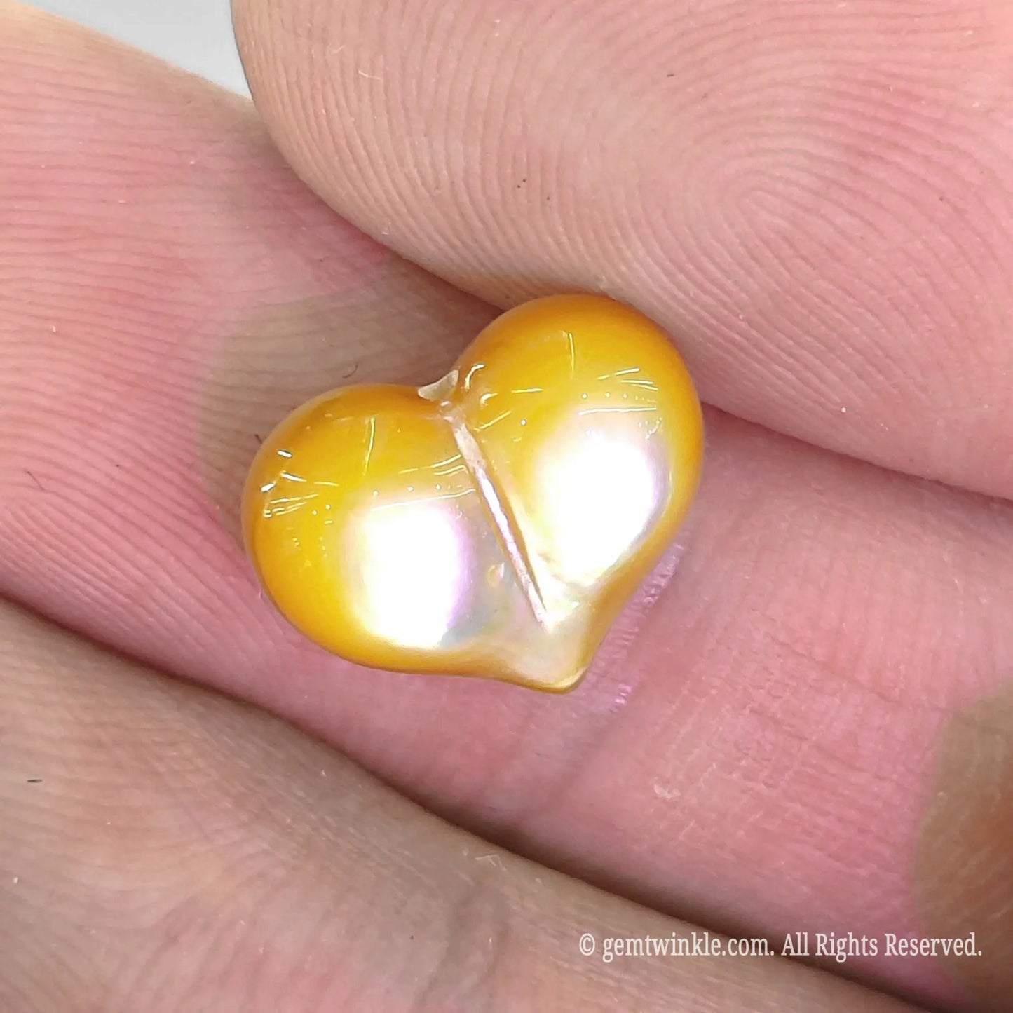 Yellow mother of pearl 12mm heart bead close up view showing carved center line and iridescent surface