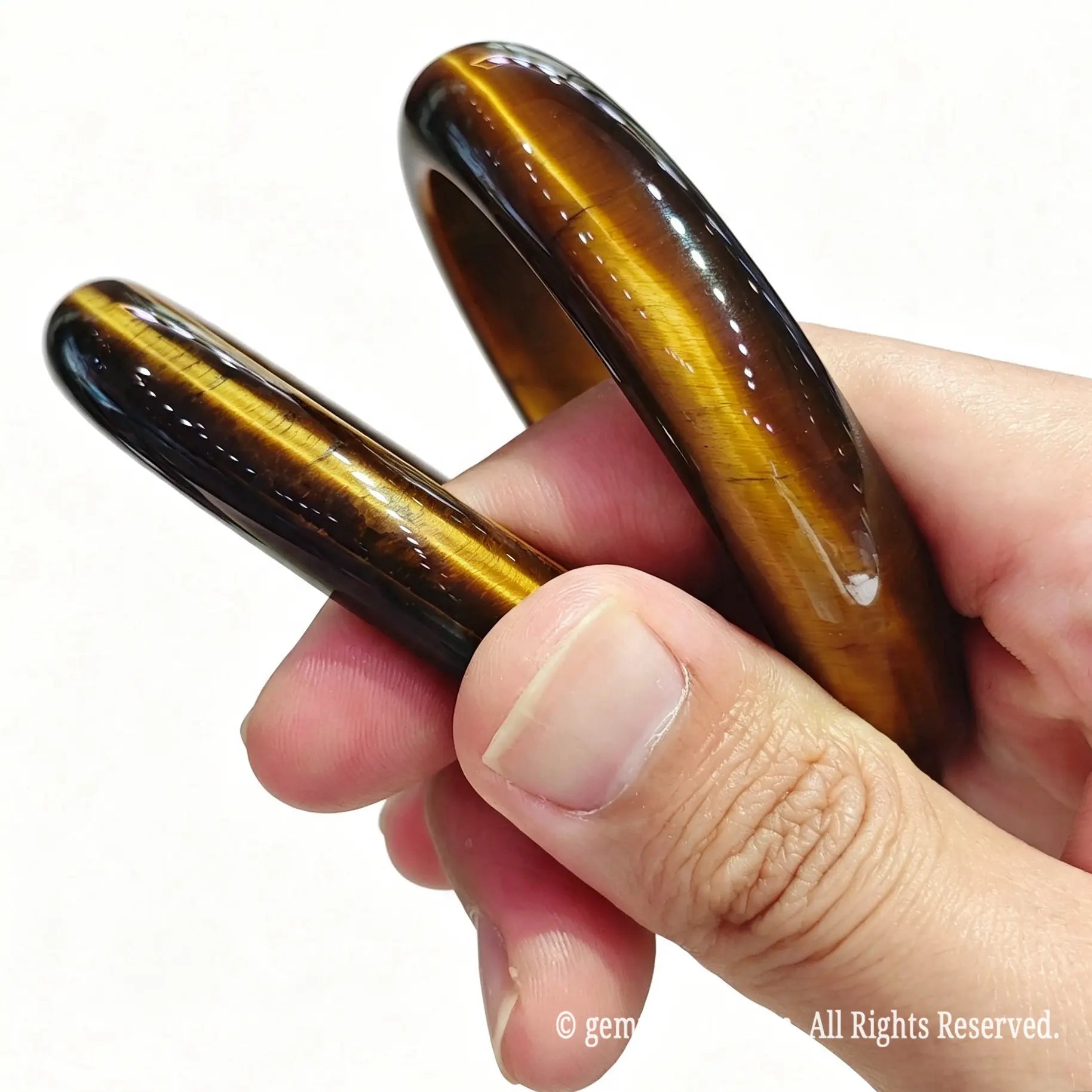 Pair of solid natural yellow tiger eye bangles held in hand showcasing silky chatoyant light reflections