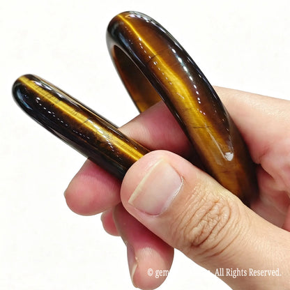 Pair of solid natural yellow tiger eye bangles held in hand showcasing silky chatoyant light reflections