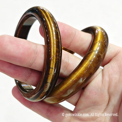 Stacked golden tiger eye gemstone bangles resting in hand displaying silky cat eye reflections and glossy polish