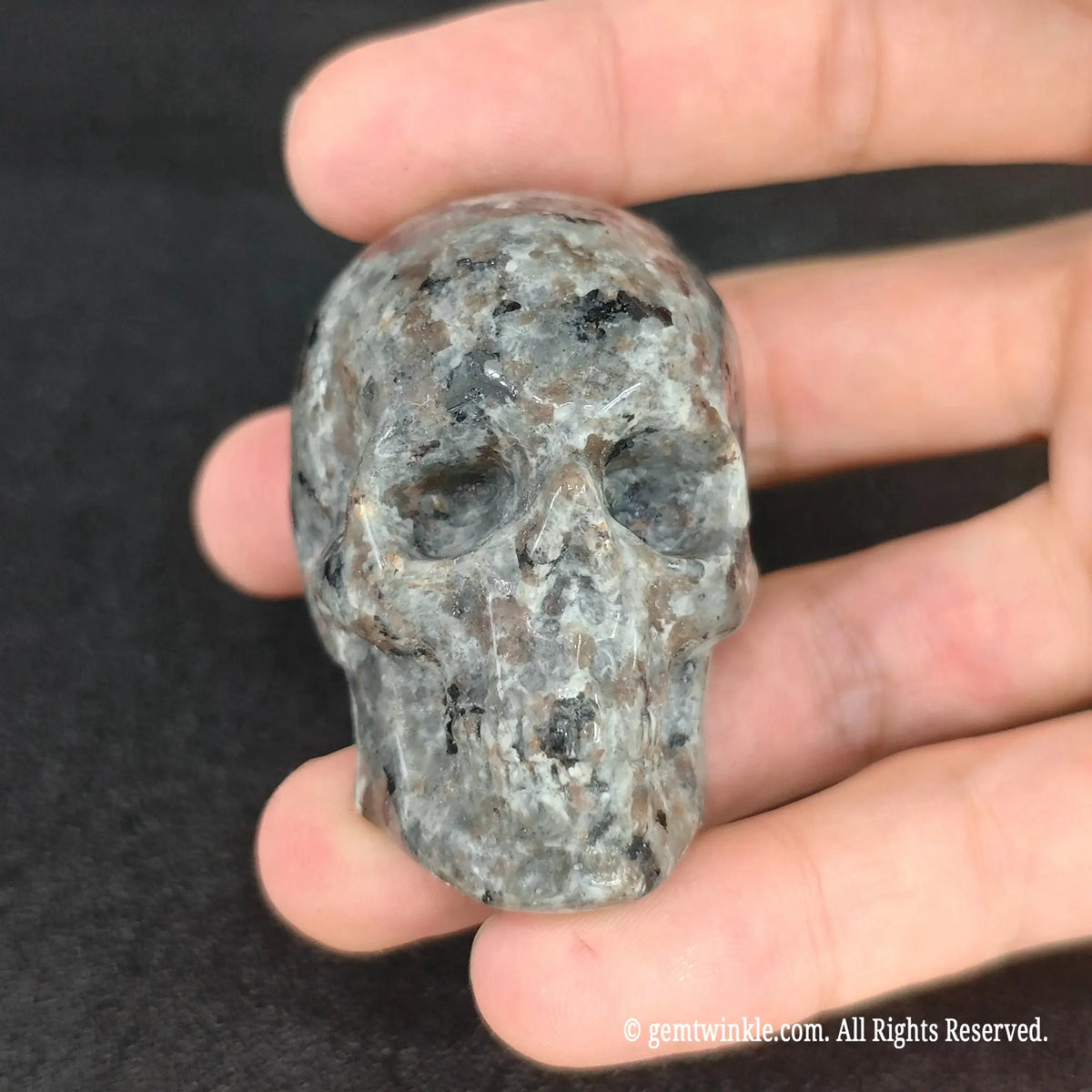 Front view of yooperlite crystal skull sculpture held in palm displaying carved eye sockets and nasal cavity